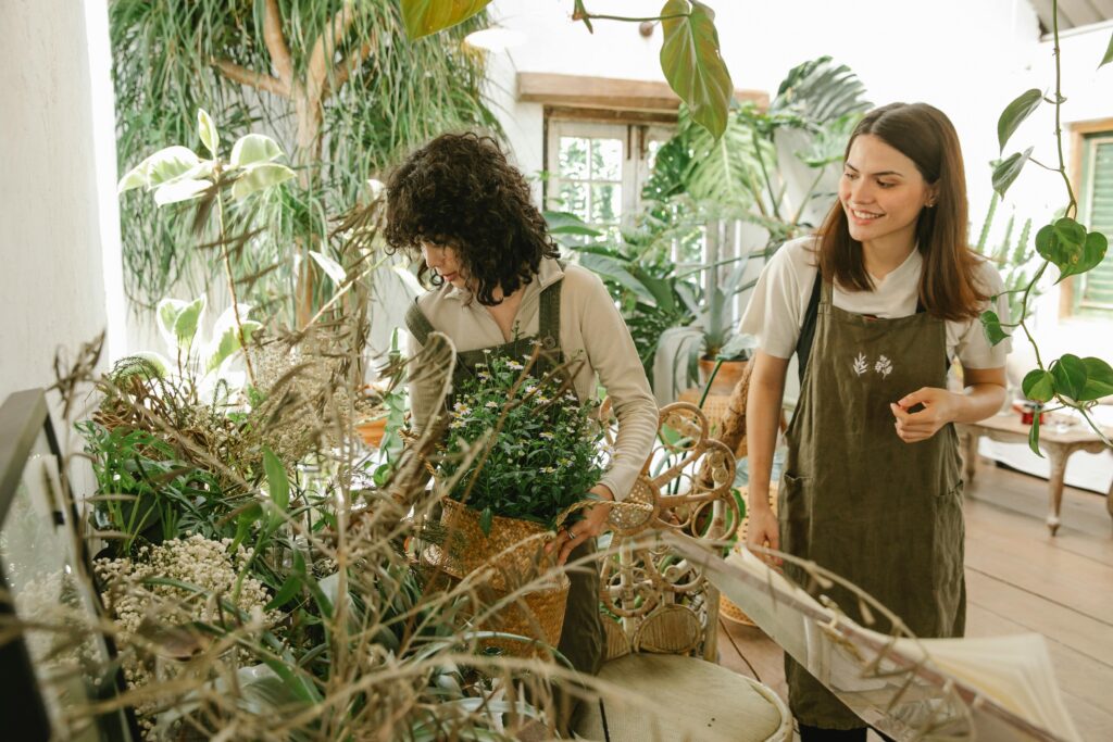 Two female florists arranging green plants in a brightly-lit shop, smiling and enjoying their work.